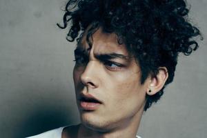 portrait de une Beau gars avec frisé cheveux sur une gris Contexte blanc T-shirt fermer modèle photo