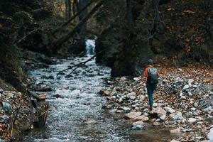 femme touristique avec une sac à dos marchait le long de le banque près le rivière, une courant de l'eau et grand des arbres photo