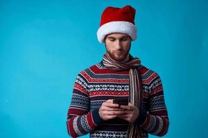 Beau homme dans une Père Noël chapeau avec une téléphone dans le sien mains bleu Contexte photo