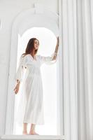 femme dans une blanc robe dans le ouverture dans le forme de un cambre posant photo