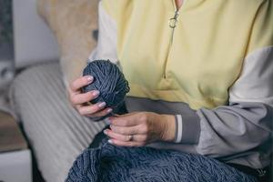 fermer femelle mains tenir une Balle de fil dans leur mains et démêler un vieux tricoté produit photo