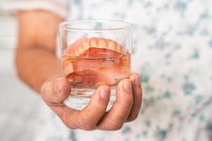 asiatique Sénior femme patient en portant et la lessive dentier dans l'eau nettoyant verre pour bien mastication. photo