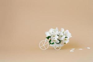 une vélo jouet avec blanc fleurs sur une beige Contexte. le concept de fête, bannière. copie espace. le concept de le début de printemps et le vacances photo