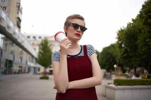 femme avec court cheveux sur le rue dans des lunettes de soleil avec une boisson photo