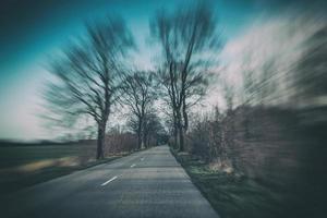 vieux étroit asphalte route avec des arbres sur le côté de le route pendant une voiture balade dans de bonne heure printemps photo