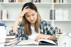 une étudiante asiatique a de l'anxiété à cause des examens, les femmes se préparent aux tests et apprennent les leçons à la bibliothèque. stress, désespoir, hâte, incompréhension lecture, découragement, attente, connaissance photo