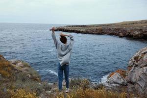 jolie femme dans une gris chandail des stands sur une rocheux rive la nature relaxation concept photo