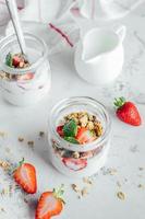 deux pots avec savoureux parfaits fabriqué de granola, des fraises et yaourt sur blanc marbre tableau. photo