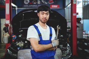 portrait de une sur de soi asiatique Masculin mécanicien à une garage. moteur entretien entretien vérification le état de le auto. réparation un service concept. photo