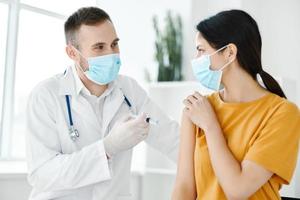 une laboratoire assistant dans une médical robe détient une seringue dans le sien main et une patient convoitise vaccination photo