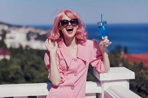 Jeune femelle dans une rose robe dans des lunettes de soleil avec une cocktail ensoleillé journée photo