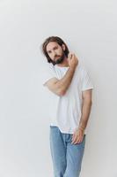 une homme dans une blanc T-shirt et bleu jeans des stands contre une blanc mur et pose photo