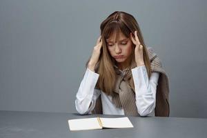 triste fatigué Jeune blond étudiant Dame pigiste dans chaud chandail toucher tête tous les deux mains séance à lieu de travail dans gris moderne Accueil bureau. éloigné emploi, éducation et carrière profession concept. copie espace photo