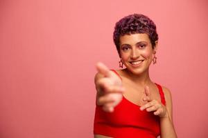 mode portrait de une femme avec une court la Coupe de cheveux de violet Couleur et une sourire avec les dents dans une rouge Haut sur une rose Contexte dansant Heureusement photo