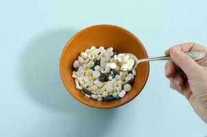 une main boules en haut médicament de une bol. des médicaments avec une cuillère. assiette avec médicaments sur une bleu Contexte. photo