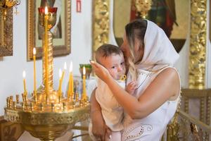 orthodoxe Baptême. mère et enfant dans une église par chandelle. femme avec une bébé dans le temple. photo