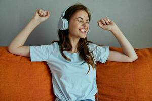 magnifique femme écoute à la musique avec écouteurs sur le Orange canapé appartements photo