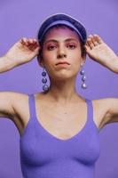 portrait de une sportif mode femme posant dans une violet des sports costume pour yoga et une transparent casquette sur une violet Contexte monochrome photo