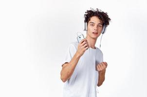 marrant gars avec frisé cheveux dans une blanc T-shirt écoute à la musique La technologie divertissement photo