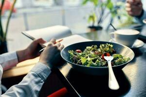 délicieux nourriture salade dans une assiette fourchette bloc-notes avec le une inscription et femme dans chemise café intérieur photo