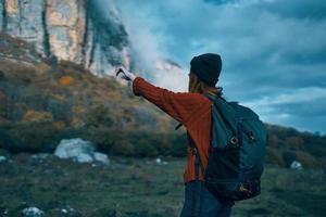 femme voyageur dans une chandail avec une sac à dos sur sa retour dans l'automne dans le montagnes sur la nature et ciel des nuages photo