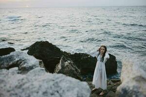 femme dans blanc robe avec humide cheveux sur le océan des pierres photo