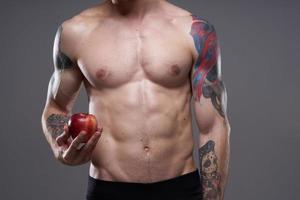 Masculin athlète avec un Pomme dans le sien mains et tatouage cubes sur le sien estomac biceps presse photo