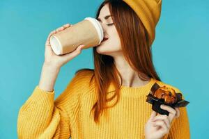 femme dans une Jaune chandail et casquette avec une tasse de café petit gâteau dans sa mains une casse-croûte photo