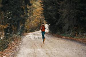 content Voyage avec une sac à dos dans une chaud chandail, pantalon et bottes des promenades le long de le route dans le l'automne forêt photo