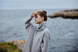 portrait de une femme dans une gris chandail des stands sur une rocheux rive la nature femelle relaxant photo