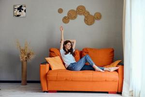 de bonne humeur femme sur le Orange canapé dans le du repos pièce posant inchangé photo