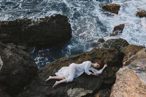 sensuel femme dans une blanc robe mensonge sur une pierre dans une blanc robe paysage photo