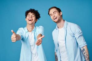 Jeune les mecs dans le même chemises et t-shirts sont faire des gestes avec leur mains sur une bleu Contexte copains photo