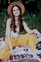 magnifique Jeune fille fermer regards dans le caméra dans une chapeau portant un éco hippie en plein air, magnifique sourire avec les dents dans le le coucher du soleil lumière photo