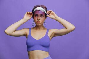 portrait de une sportif mode femme posant dans une violet des sports costume pour yoga et une transparent casquette sur une violet Contexte monochrome photo