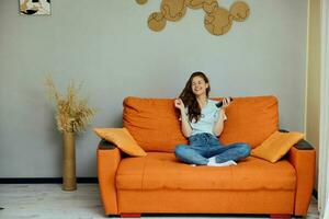 portrait de une femme bavardage sur le Orange canapé avec une téléphone intelligent inchangé photo