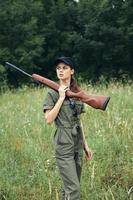 femme sur la nature avec une pistolet dans le sien mains à la recherche à le côté vert salopette Frais air photo