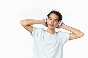 content aux cheveux bouclés gars dans écouteurs et dans une blanc T-shirt écoute à la musique et détient le sien mains près le sien visage photo