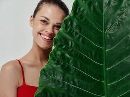 femme dans une rouge maillot de bain avec fermé yeux penché sa visage sur une vert feuille de une paume arbre photo