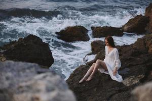 femme avec humide cheveux est assis sur une rocheux pierre nuageux temps vagues photo