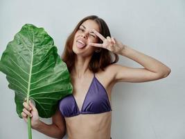 joyeux femme montrant langue dans maillots de bain vert feuille tropiques isolé Contexte photo