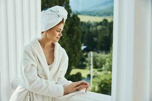 attrayant Jeune femme avec une serviette sur mon tête dans une blanc peignoir de bain rester sur le balcon dans une Hôtel inchangé photo