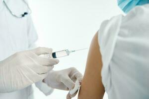 médecin dans protecteur gants injecte une vaccin dans le épaule de une femme patient dans une hôpital convoitise photo