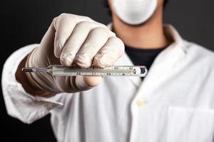 Médecin en blouse blanche avec des gants et un masque médical tient une seringue avec un traitement médicamenteux prévention des maladies vaccination photo