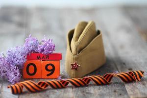 en bois calendrier avec russe texte mai 9, garnison casquette, George ruban et une bouquet de lilas sur une en bois Contexte. la victoire journée. photo