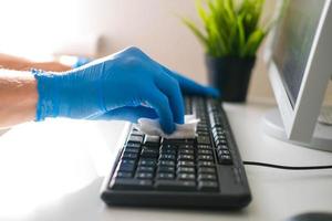 Masculin mains dans caoutchouc gants essuyer le clavier de le ordinateur. désinfection dans le Bureau pendant covid-19 photo