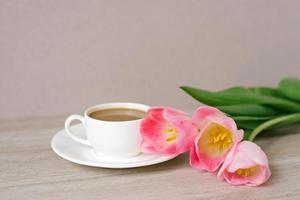 café avec Lait dans une blanc porcelaine tasse et soucoupe, une bouquet de printemps rose tulipes. de la mère jour, la Saint-Valentin jour, Pâques. le concept de printemps photo