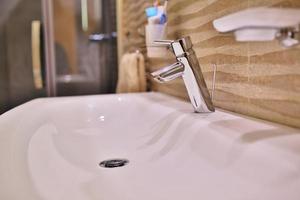 Mélangeur de robinet de luxe sur un évier blanc dans une belle salle de bain intérieure grise. Vue rapprochée du joli robinet en métal dans la salle de bains moderne photo