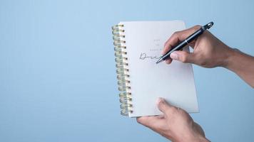 homme main en portant une stylo et l'écriture sur une carnet isolé sur bleu Contexte. photo