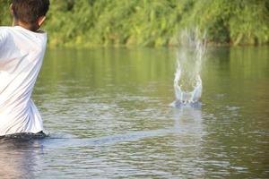 asiatique garçon est dépenses le sien temps libre par plongée, natation, lancement rochers et contagieux poisson dans le rivière Heureusement, loisir et bonheur de les enfants concept, dans mouvement. photo